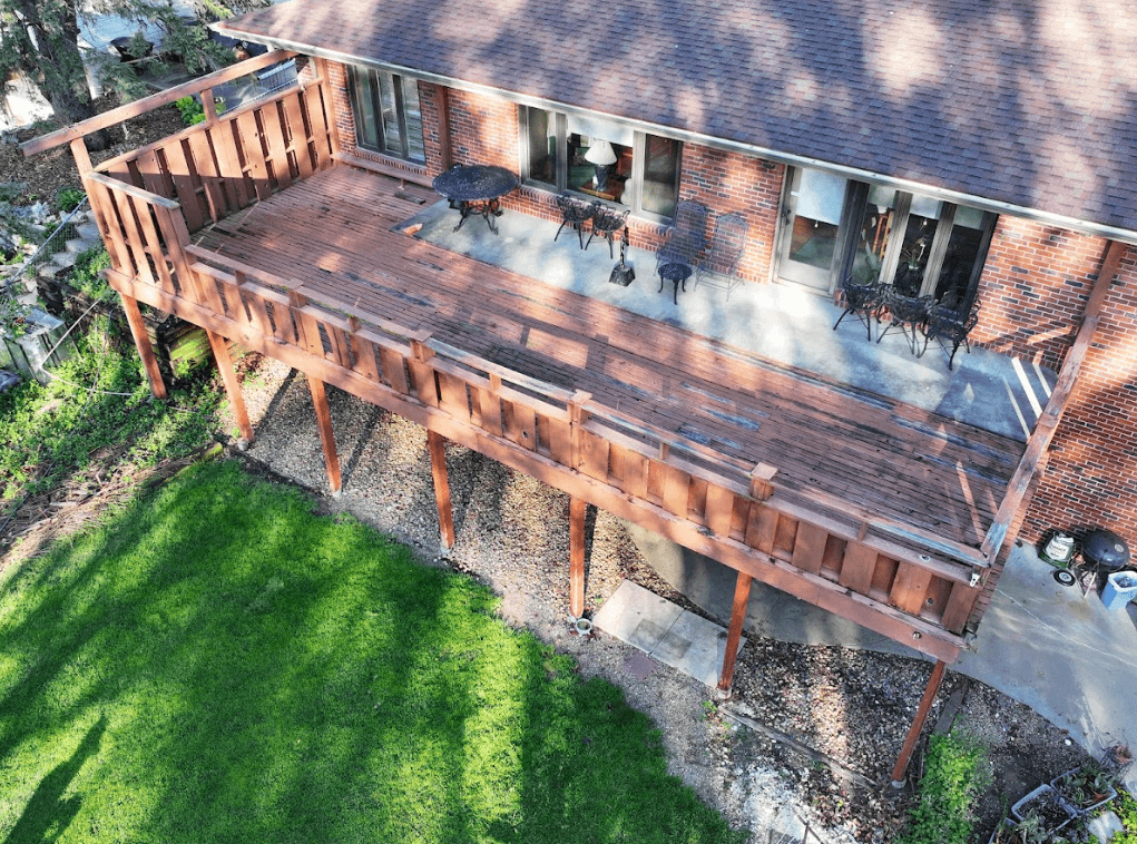 A weathered, deteriorating wooden deck attached to a brick house.